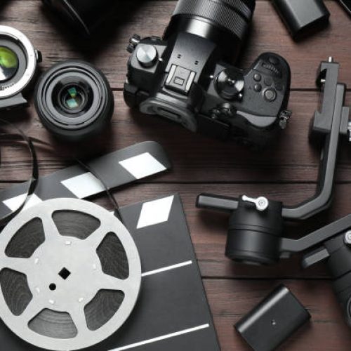 Flat lay composition with camera and video production equipment on brown wooden background